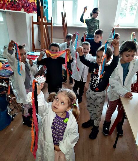 Dzieci z instruktorkę, trzymające dłonie w górze z pracami wykonanymi na zajęciach
