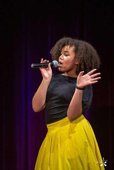 Dziewczyna z mikrofonem w żółtej spódniczce i czarnej bluzce