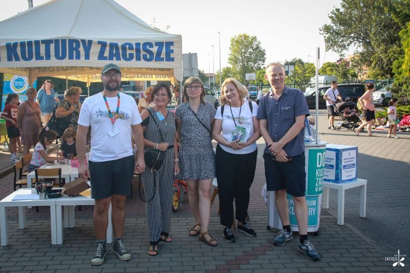 Uśmiechnięci kobiety i mężczyźni, w tle namiot Dom Kultury Zacisze