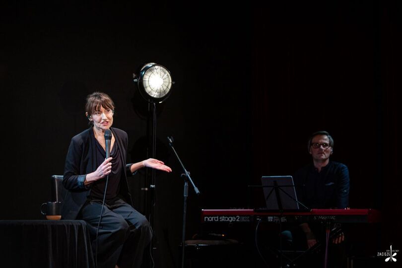 Zdjęcie: kobieta w czarnym stroju z mikrofonem, w tle pianista