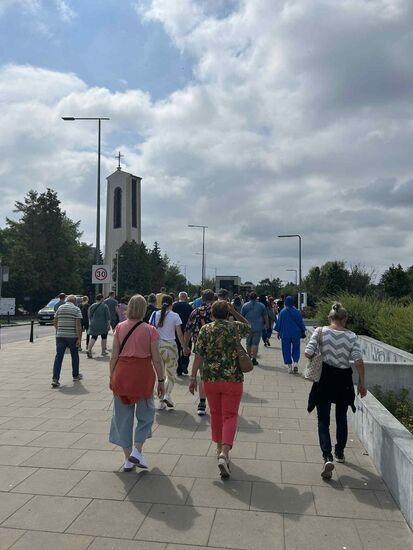 Zdjęcie: spacerująca grupa ludzi, w tle wieża kościoła z krzyżem