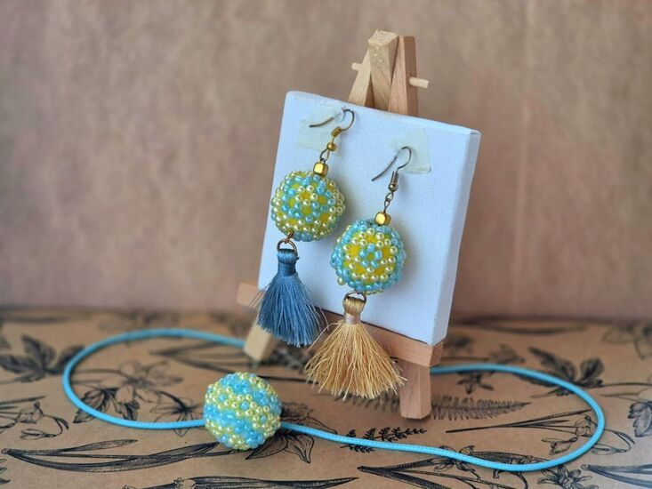 Zdjęcie: kolczyki z koralików i sznurków zawieszone na mini sztaludze, przed nimi naszyjnik z koralikową, błękitną kulką