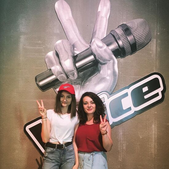 Zdjęcie: Kobieta i nastolatka, w tle ściana z grafiką Voice i mikrofonem
