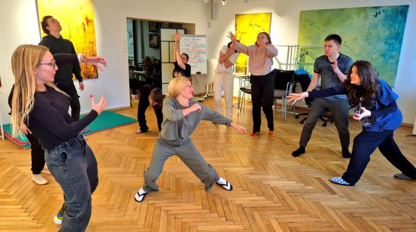 Zdjęcie: grupa osób w choreografii na parkiecie, w tle kolorowe obrazy