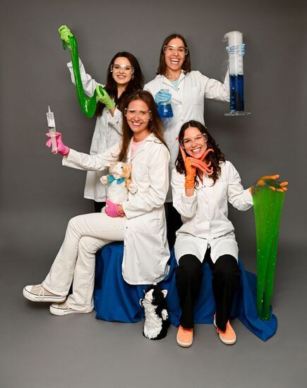 Zdjęcie: cztery uśmiechnięte kobiety z probówkami, kolorowymi substancjami, w białych fartuchach, w okularach ochronnych