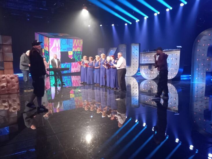 Zdjęcie: Seniorki w niebieskich sukienkach i seniorzy podczas próby przed występem