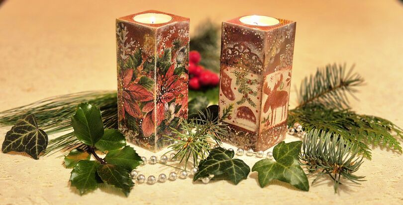 Zdjęcie: Dwa świeczniki wykonane techniką decoupage z bożonarodzeniowymi akcentami z palącymi się na górze tealight'ami stojące na elementach z igliwia, listków i sznurka z białych koralików