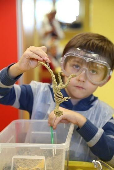 Zdjęcie: Chłopiec w ochronnych okularach trzymający dinozaura - zabawkę w dłoniach