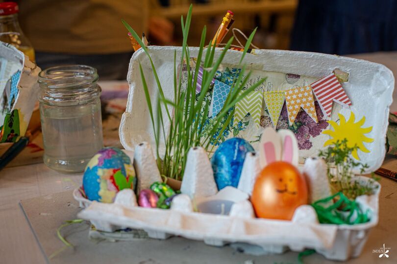Zdjęcie: Pudełko po jajkach ozdobione kolorowymi pisankami, zieloną trawą i innymi ozdobami