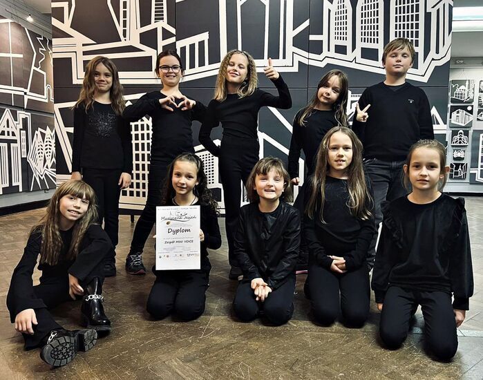 Zdjęcie: Uśmiechnięte dzieci w czarnych strojach, jedna dziewczynka trzyma dyplom