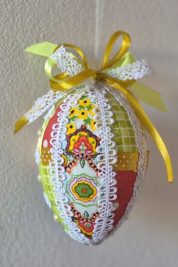 Zdjęcie: Pisanka w żółto-białej kolorystyce z czerwonymi akcentami ozdobiona kolorowymi skrawkami tkanin, koronką, wstążkami oraz koralikami