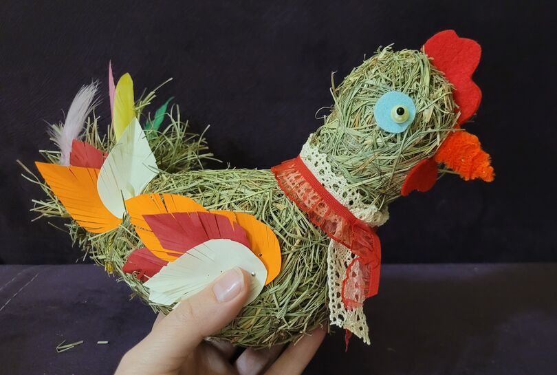 Zdjęcie: kura ze słomy ozdobiona kolorowymi elementami z materiału, widoczna ręka trzymająca całość