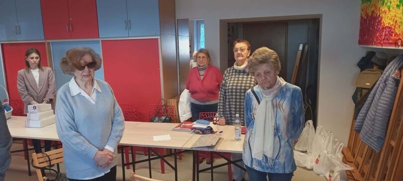 Zdjęcie czterech osób starszych i jednej młodszej stojących przed stołami