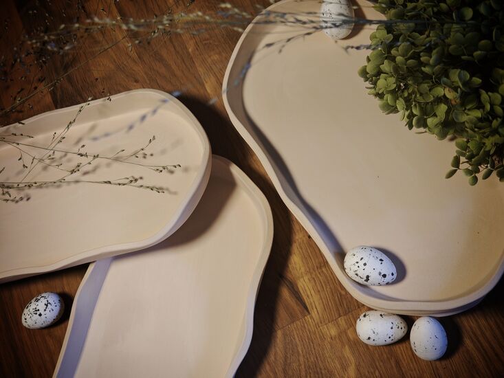Zdjęcie: Trzy ceramiczne podstawki i trzy malutkie jajka na drewnianym blacie, widoczny fragment bukszpanu
