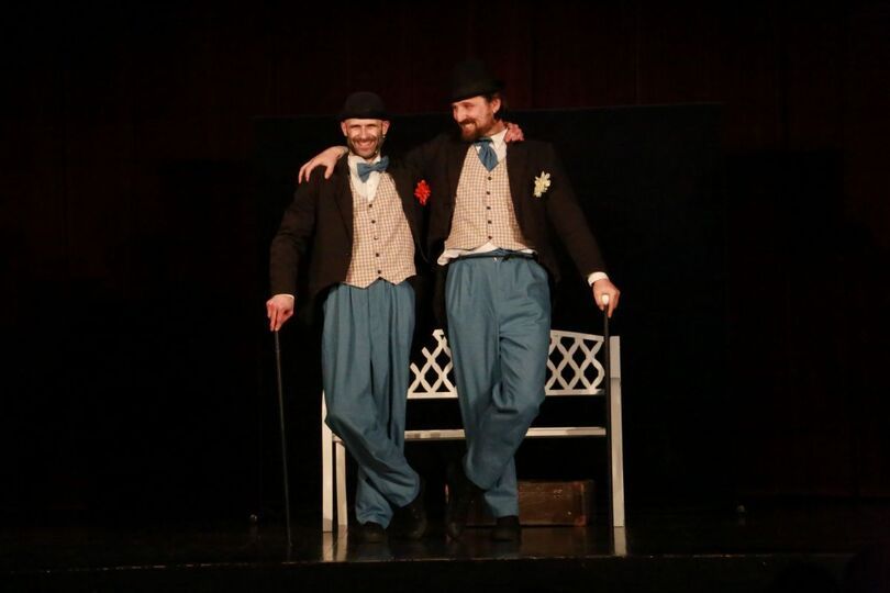 Zdjęcie: dwóch uśmiechniętych mężczyzn na scenie trzymających się za ramię, z tyłu biała ławeczka