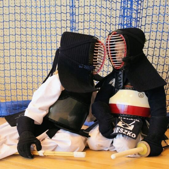 Zdjęcie: dwóch młodych zawodników siedzących na podłodze w tradycyjnych strojach Kendo z mieczami