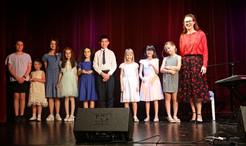 Zdjęcie: młoda uśmiechnięta kobieta z dziećmi na scenie, przed nimi odsłuch sceniczny