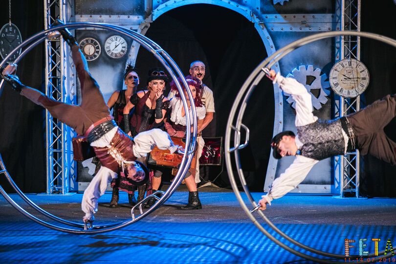 Zdjęcie: grupa osób wykonujących pokaz akrobatyczny na wielkich kołach w steampunkowej scenografii